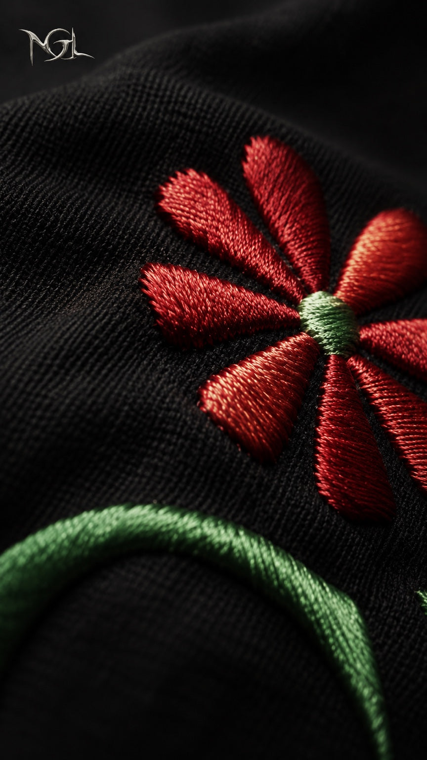 Close-up of the NGL tracksuit embroidery showing the red flower detail and green stitching on black fabric.