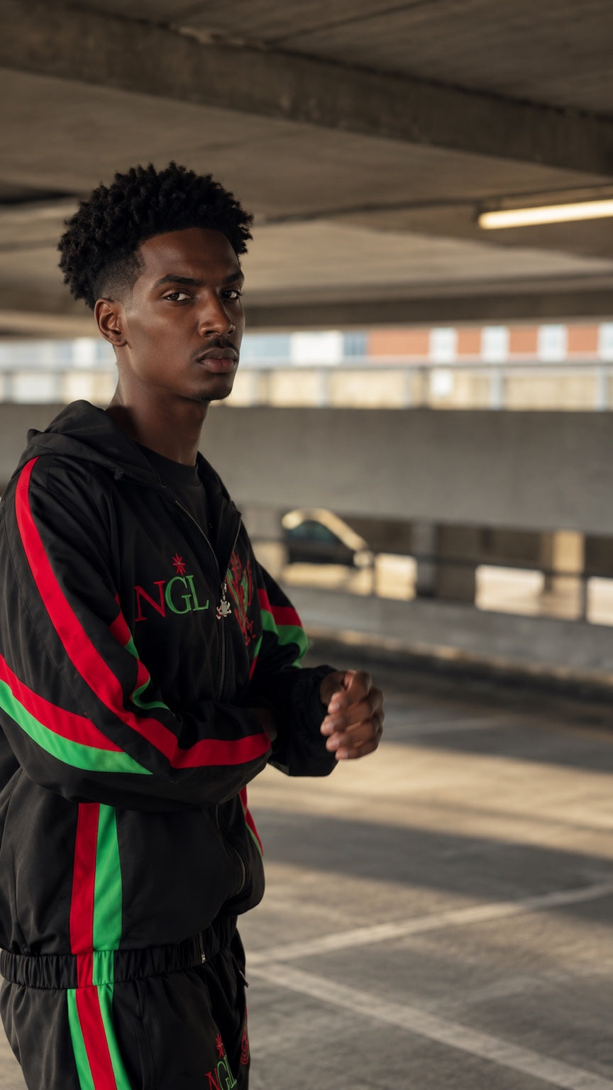 Model wearing the black NGL tracksuit in a parking structure, showing the front fit and red and green detailing.